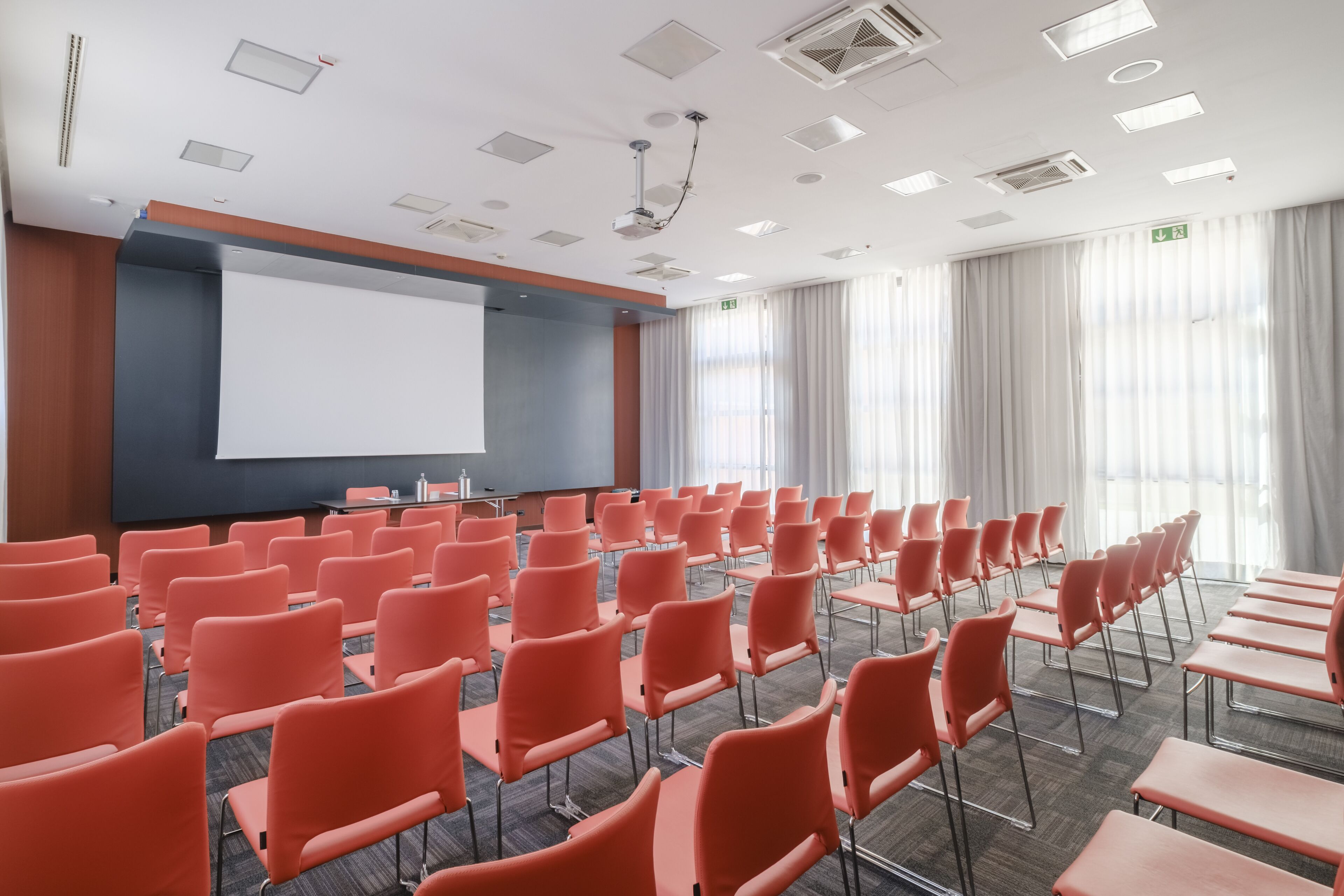 A conference room with rows of orange chairs, a large projection screen, and a whiteboard.
