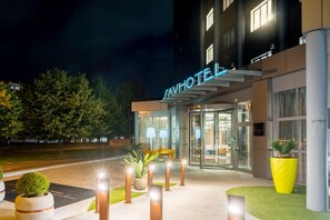 A hotel entrance with a glass facade, outdoor seating, and a well-lit entrance area.