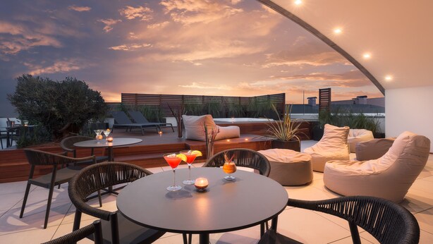 A rooftop terrace with a round table, chairs, and a sofa. There are drinks on the table, and the terrace overlooks a cityscape. - Savhotel Fiera Bologna (Bologna)