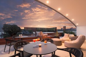 A rooftop terrace with a round table, chairs, and a sofa. There are drinks on the table, and the terrace overlooks a cityscape. - Savhotel Fiera Bologna (Bologna)