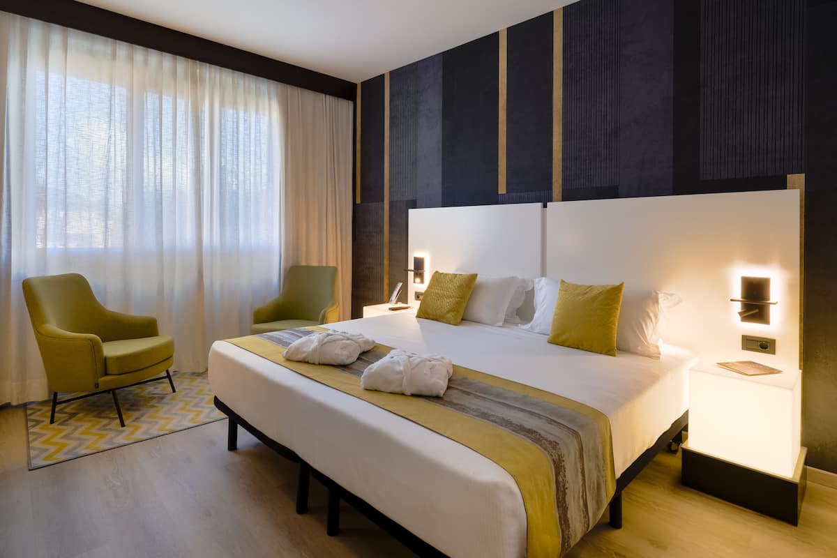 A hotel room with a large bed, a chair, a bedside table, and a nightstand.