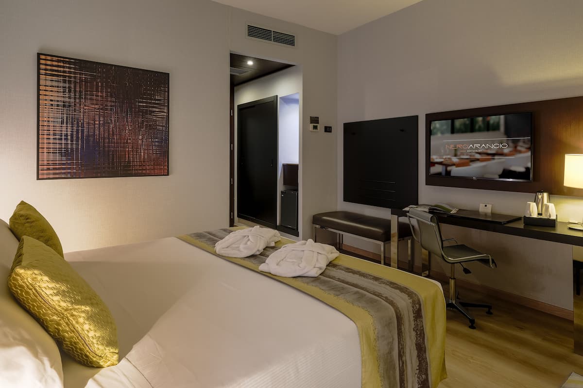 A hotel room with a bed, a desk, a TV, and a large abstract painting on the wall.