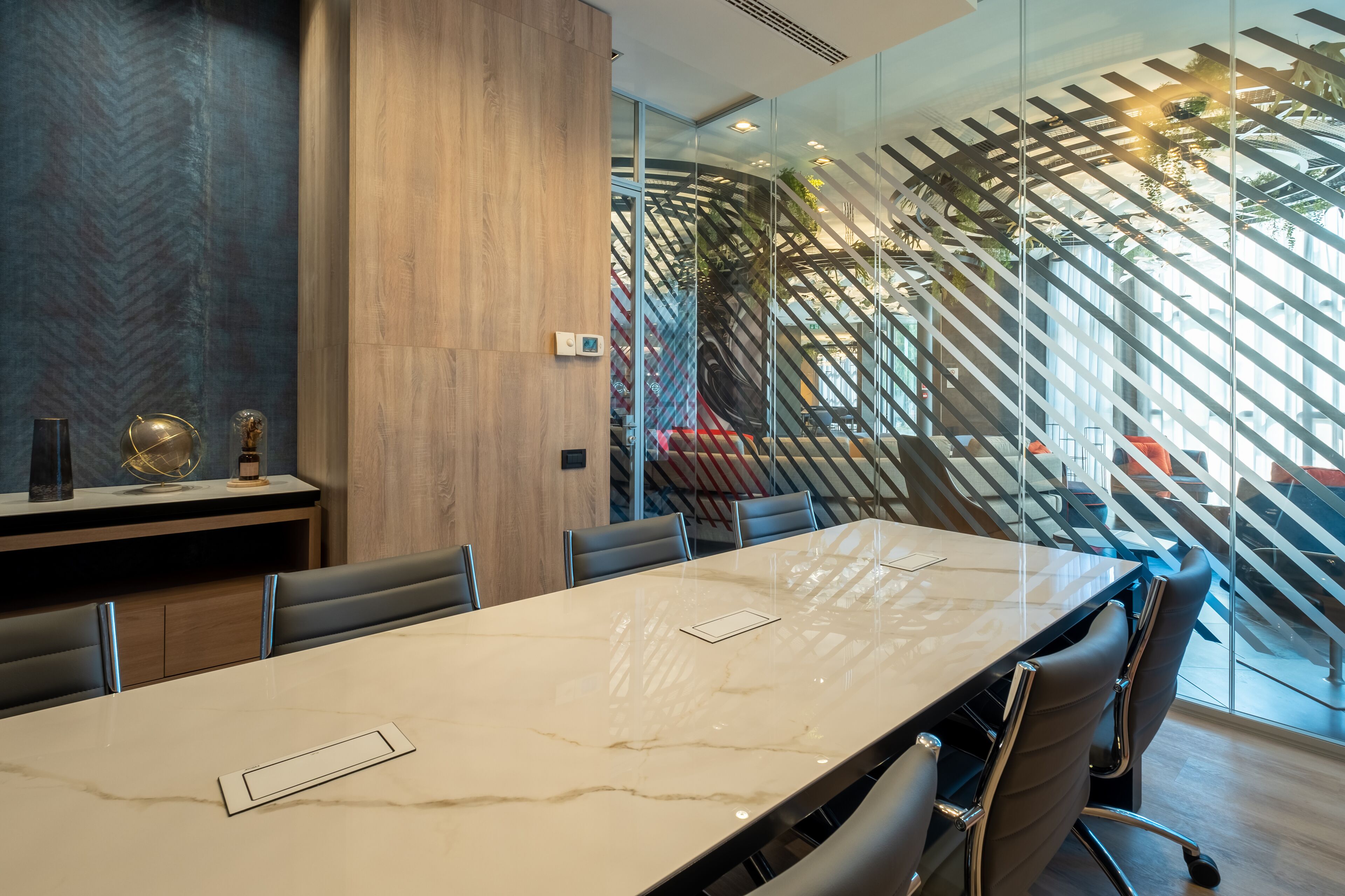 A modern conference room with a large marble table, leather chairs, and a glass partition with a geometric pattern.