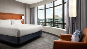 Een hotelkamer met een groot bed, een stoel, een raam met uitzicht over de stad, en een moderne lamp.