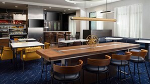 Een modern restaurant met een lange houten bar, meerdere zitgedeeltes en een keuken op de achtergrond.