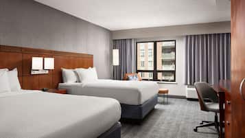 A hotel room with two beds, a desk, a chair, a lamp, and a window with curtains.