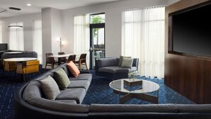 Een moderne hotel lobby met een gebogen bank, een ronde salontafel, een televisie en een eetgedeelte met gele stoelen en een tafel.