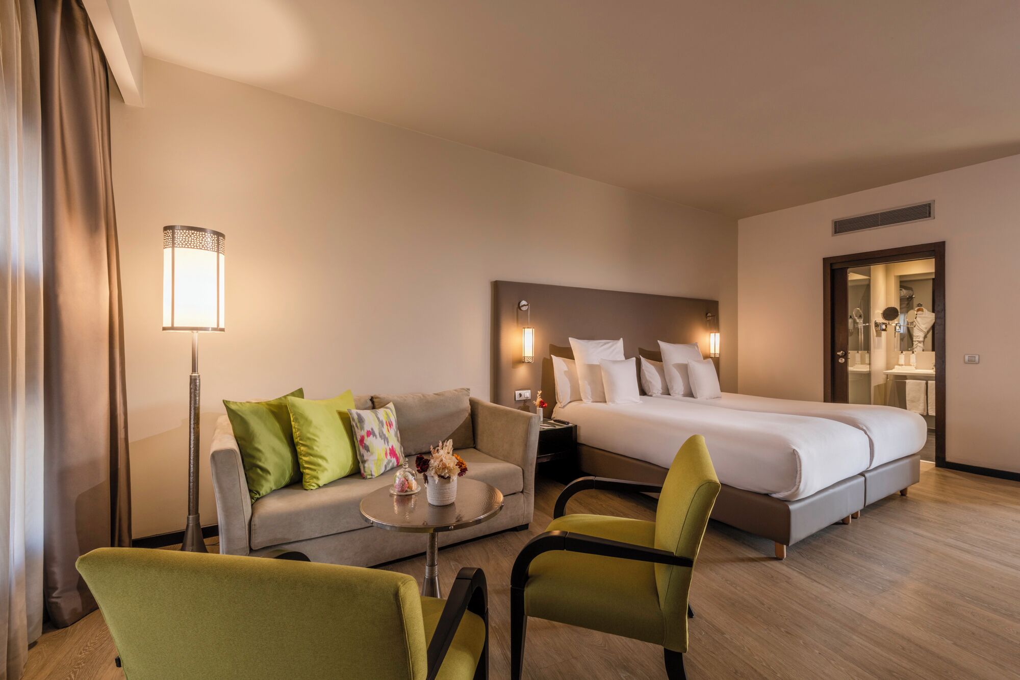A hotel room with a bed, a sofa, a chair, a small table, and a lamp.