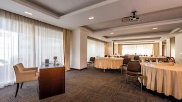 A conference room with multiple tables, chairs, a podium, and a projector.