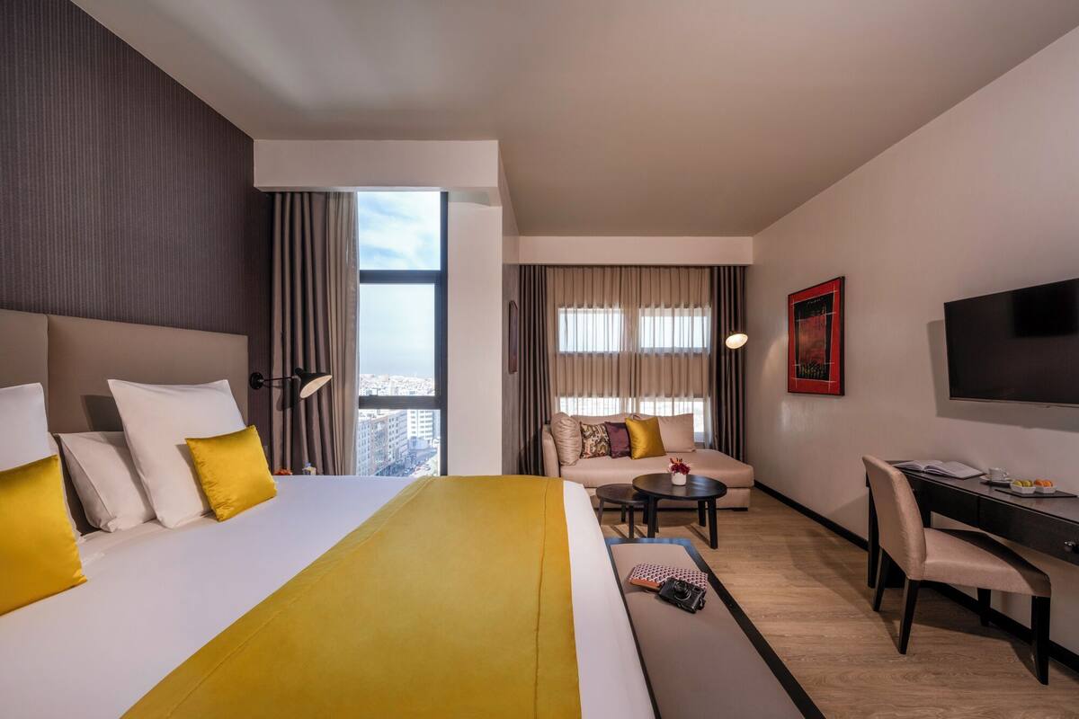 Ein Hotelzimmer mit einem großen Bett, einem Schreibtisch, einem Sessel, einem kleinen Tisch und einem Fernseher.