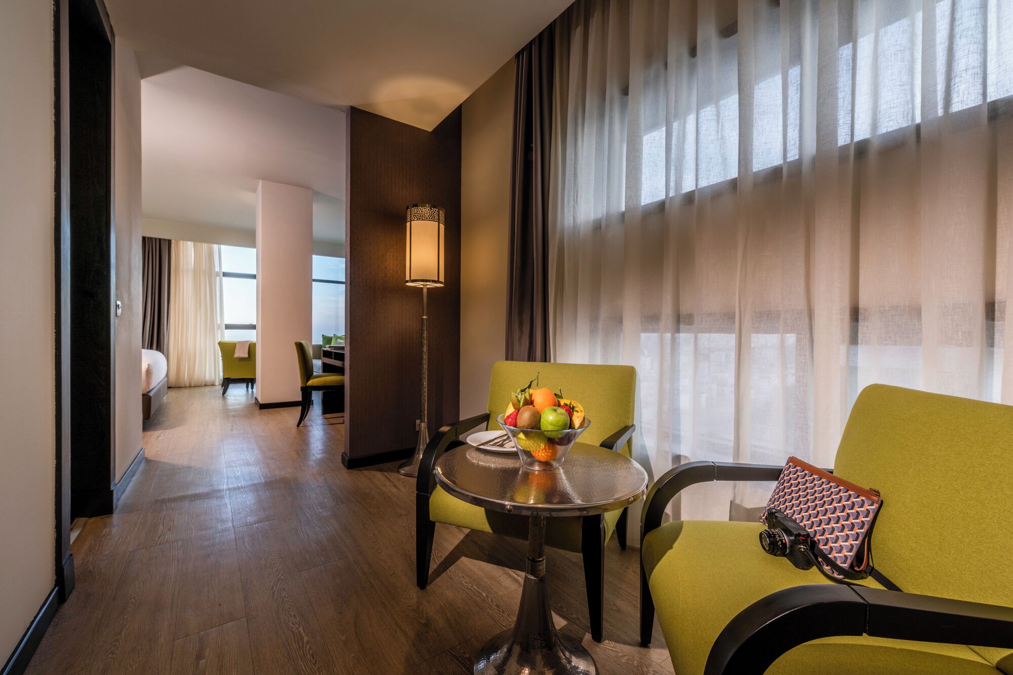 Une chambre d’hôtel comprenant un coin repas, un lit, un canapé vert et une table avec un panier de fruits.