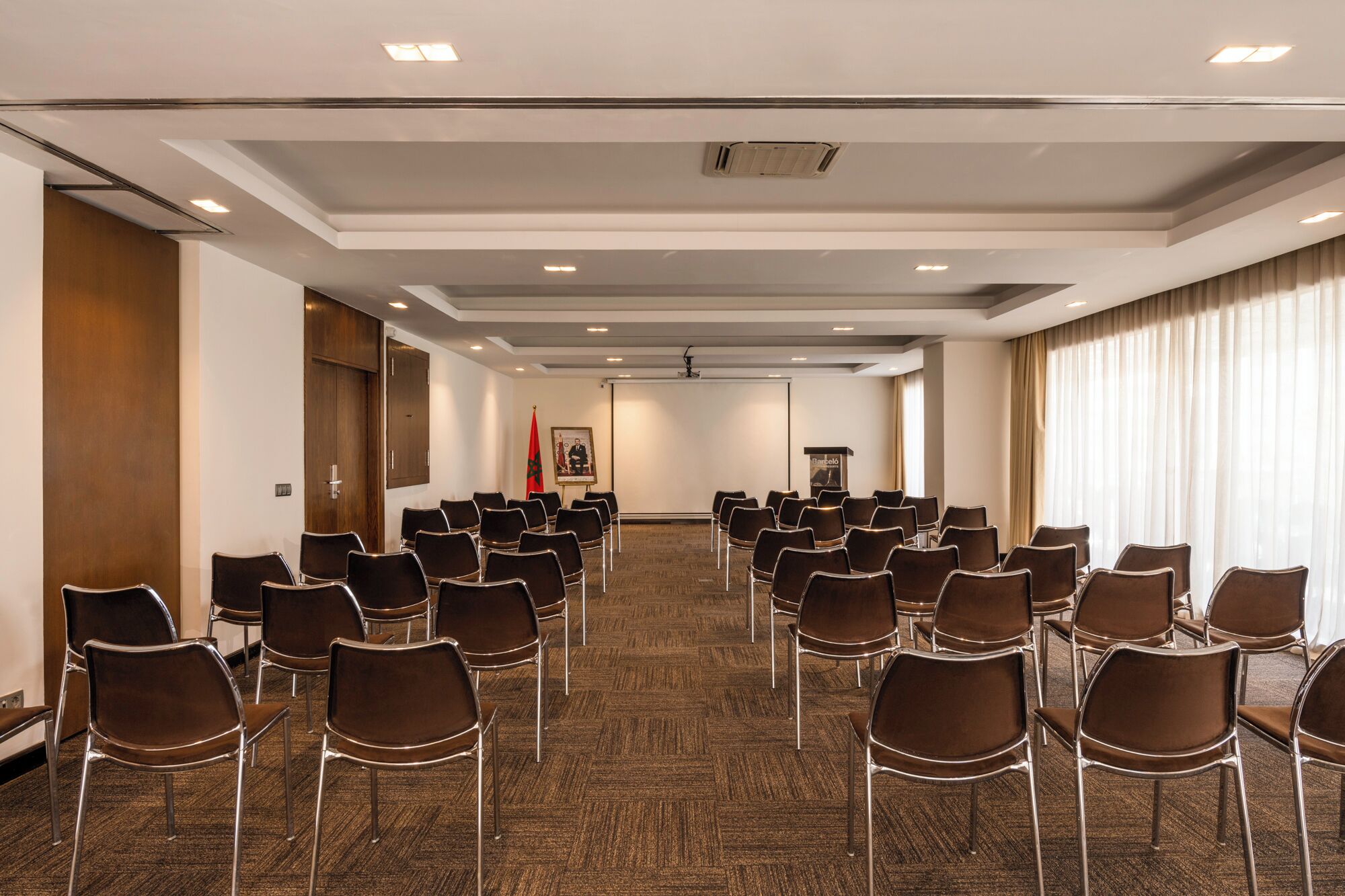 Un salón de conferencias con filas de sillas, un atril y banderas en las paredes.
