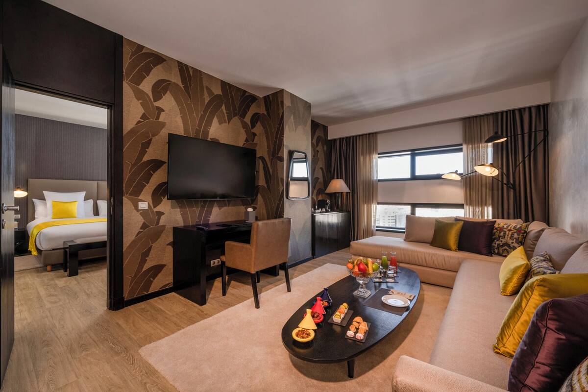 Ein modernes Hotelzimmer mit einem großen Bett, einem Flachbildfernseher, einem Schreibtisch, einer Couch und einem Esstisch mit Speisen.