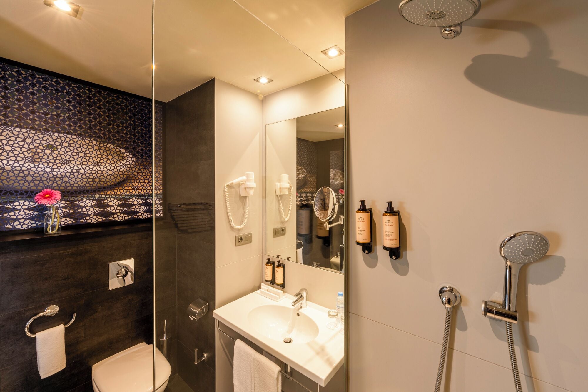 Een moderne badkamer met een glazen douchecabine, een wastafel met spiegel en toiletartikelen aan de wand.