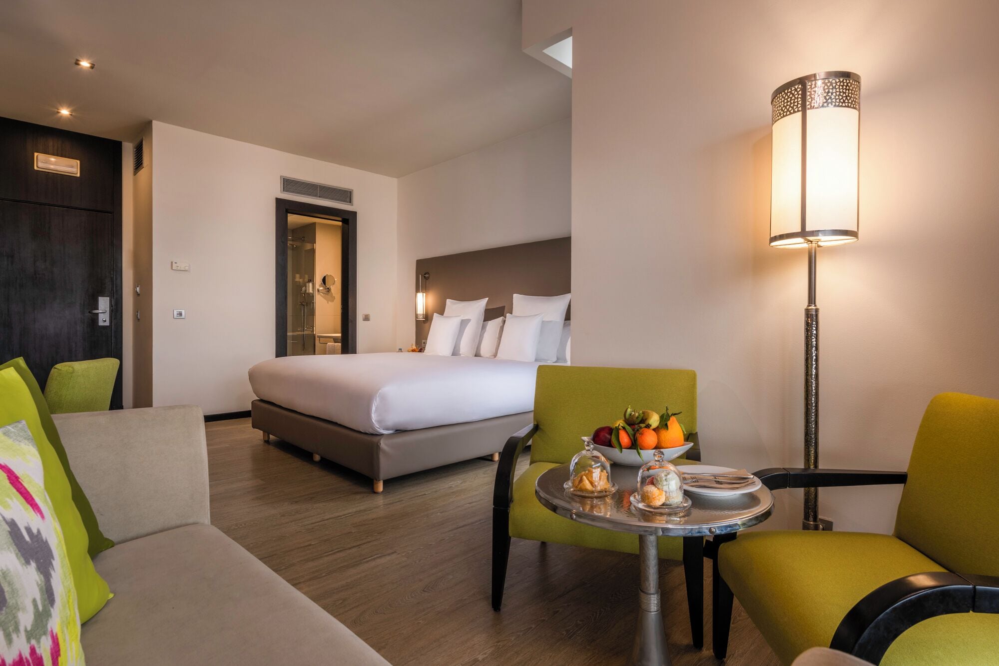 Una habitación de hotel con cama, zona de estar con mesa y lámpara.