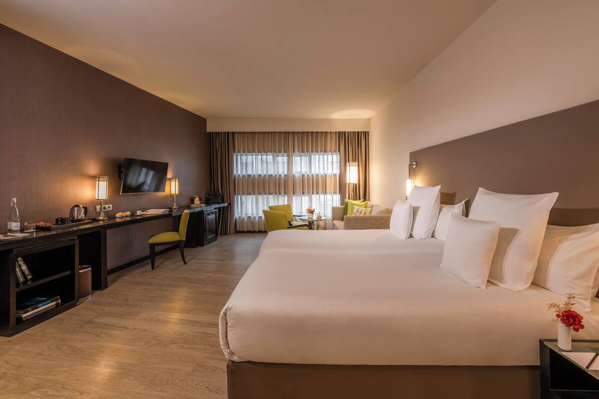 Ein Hotelzimmer mit einem großen Bett, einem Schreibtisch mit Stuhl, einem Fernseher und einem Fenster mit Vorhängen.