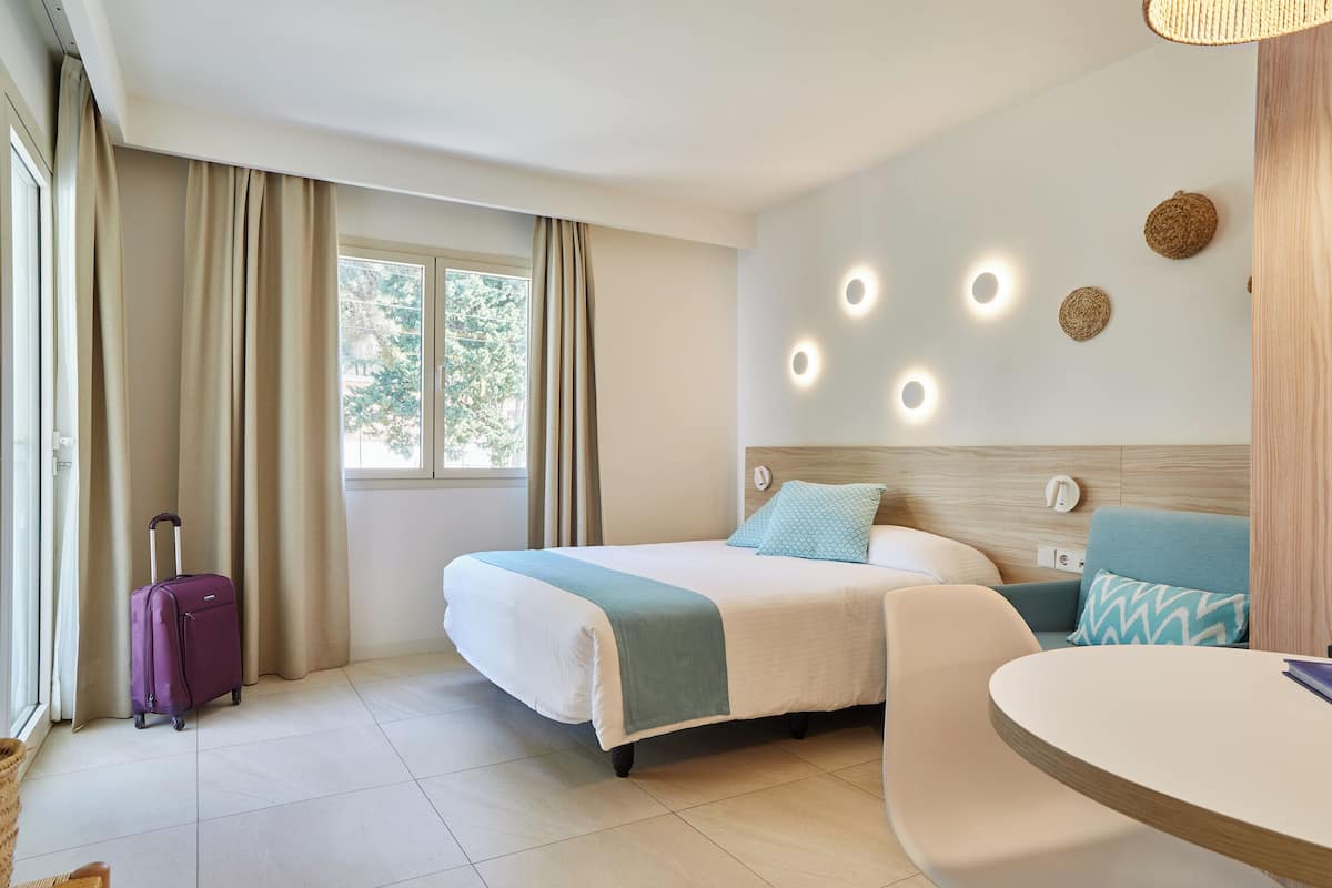 Ein Hotelzimmer mit Bett, Stuhl, Tisch und Koffer.