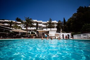 Una piscina con persone che si divertono in acqua, circondata da posti a sedere all'aperto e palme.