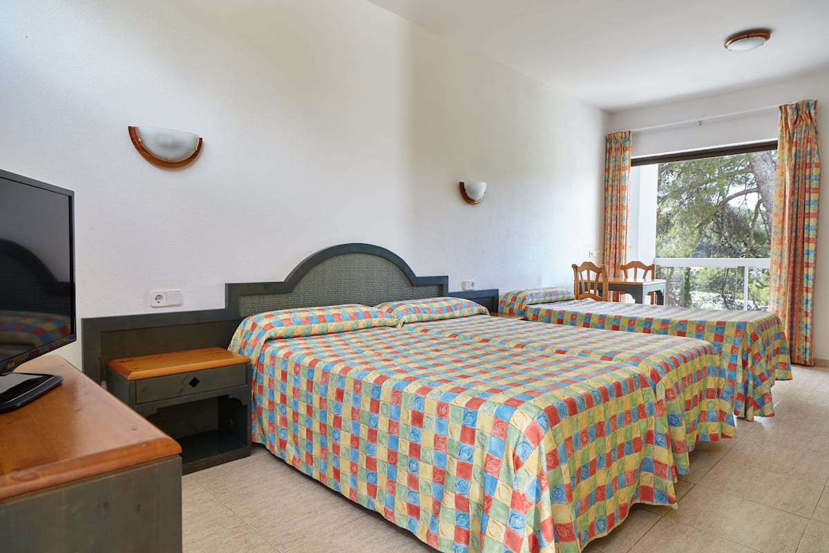 Ein Hotelzimmer mit zwei Betten, einem Schreibtisch, einem Fernseher und einem Fenster mit Vorhängen.