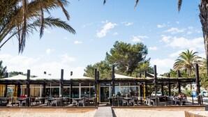 A beachside restaurant with outdoor seating, a wooden deck, and a sandy area.