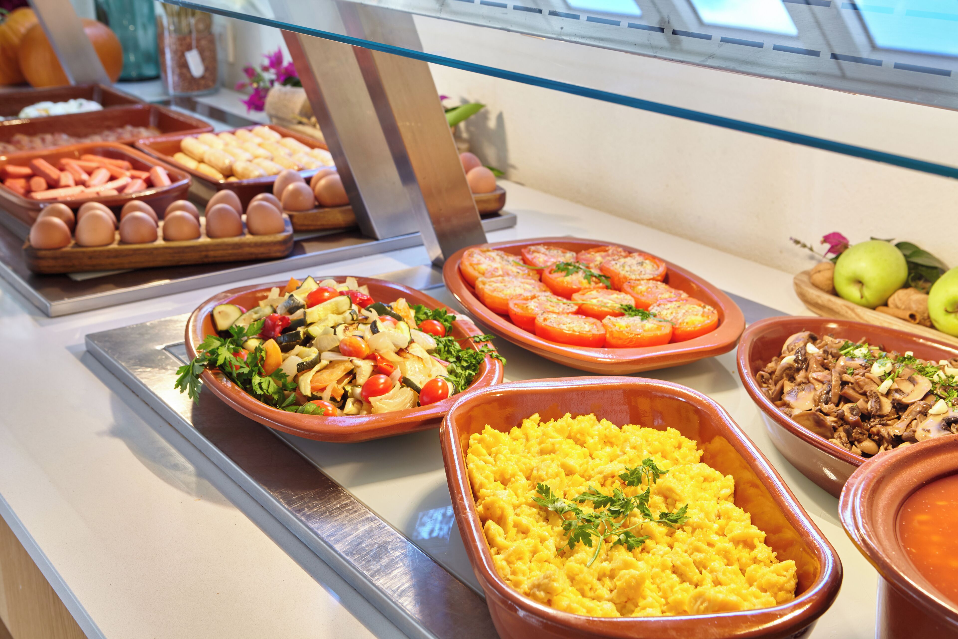 A buffet with various food options including eggs, tomatoes, and a salad.