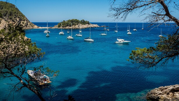 A coastal scene with clear blue waters, boats, and rocky terrain.
