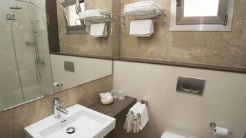 A modern bathroom with a glass shower enclosure, a white sink, a towel rack, and a toilet.