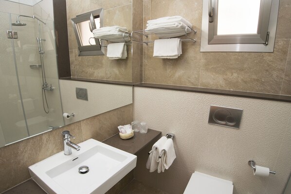 Un baño moderno con cabina de ducha de vidrio, lavamanos blanco, toallero y retrete.