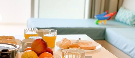 A breakfast tray with fruits, pastries, and beverages on a table in a room with a view of greenery.