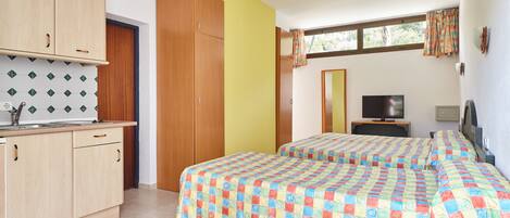 Ein Zimmer mit zwei Betten, einem Fernseher, einem kleinen Schreibtisch und einem Fenster mit Vorhängen.