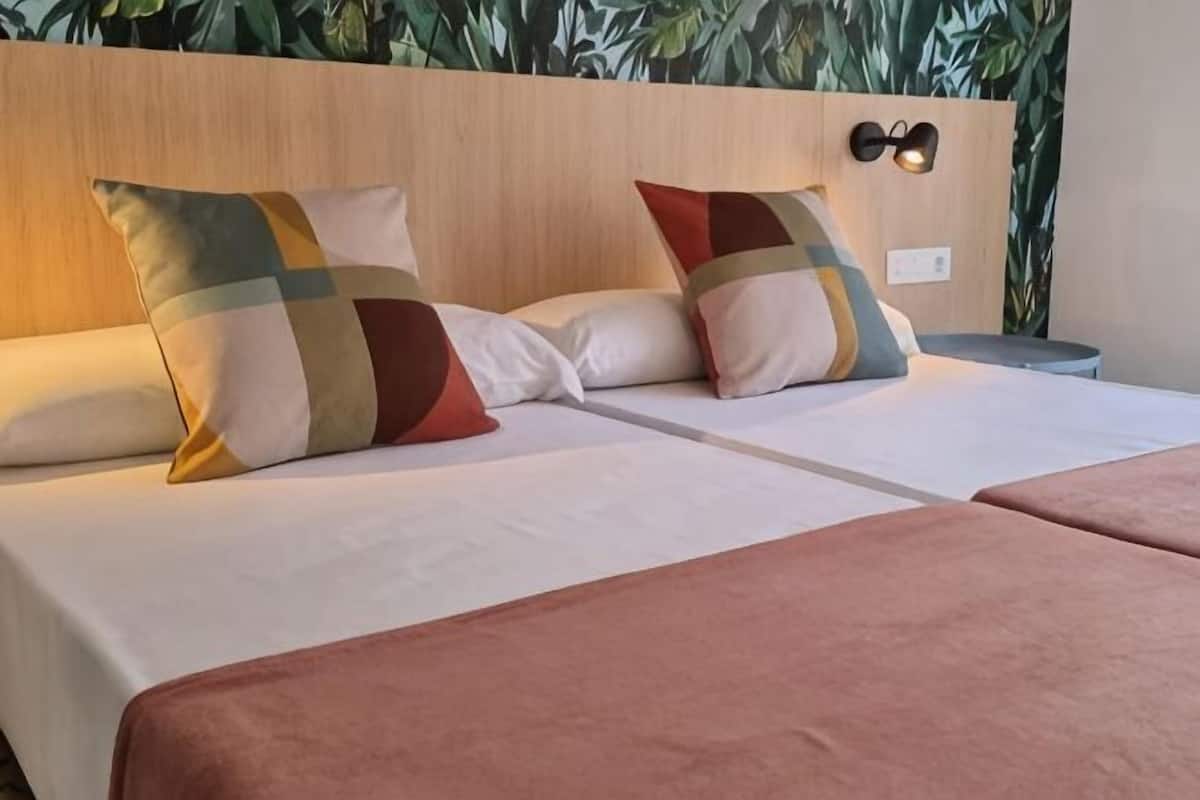 Una cama doble con almohadas estampadas, un cabecero de madera y una mesita de noche con lámpara.