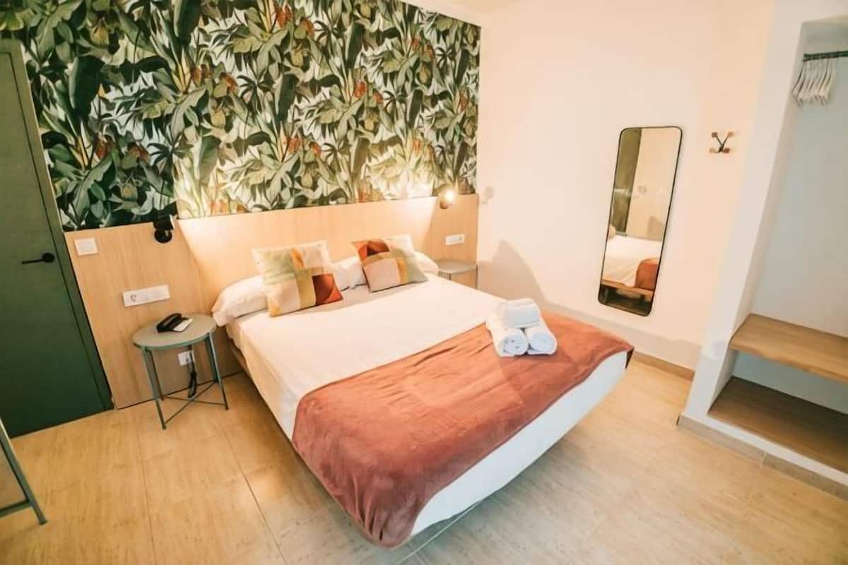 Habitación de hotel con cama, mesita de noche, espejo y una pared con un diseño de hojas.