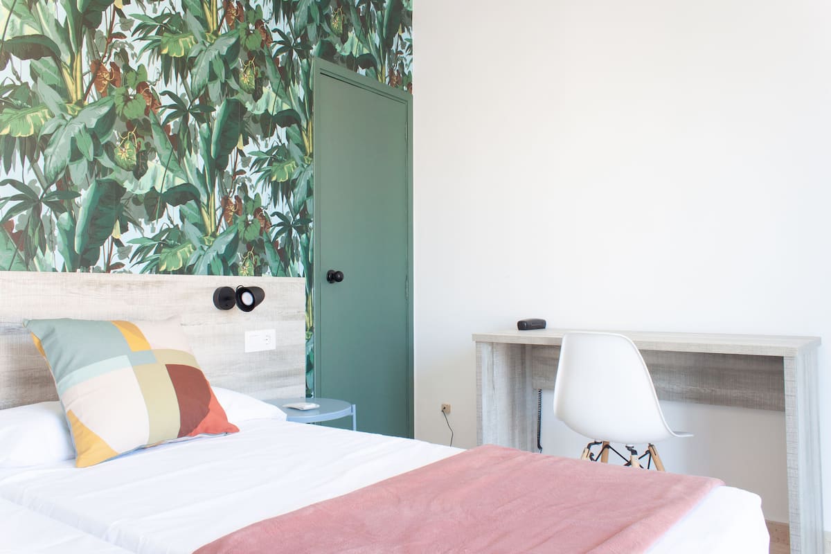 Un dormitorio con cama, mesita de noche, silla y puerta.
