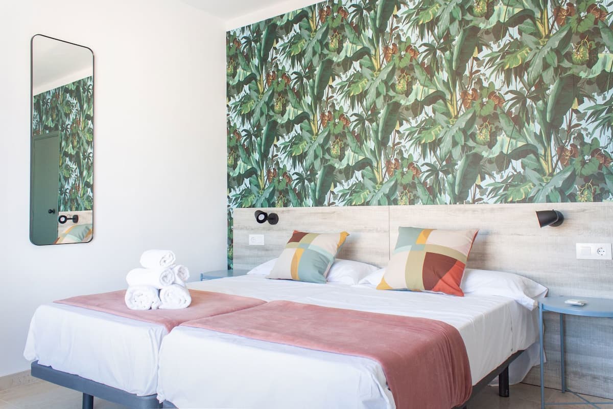 Una cama doble con cabecera de madera, un espejo y una pared con estampado de plantas tropicales.