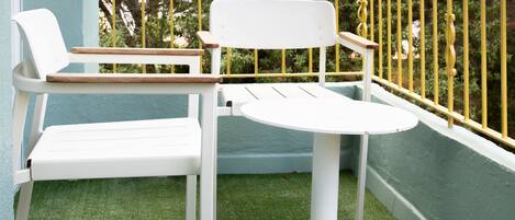 A balcony with two white chairs and a small table, surrounded by a yellow railing.