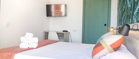 Habitación de hotel con cama, escritorio, silla, televisor y puerta.
