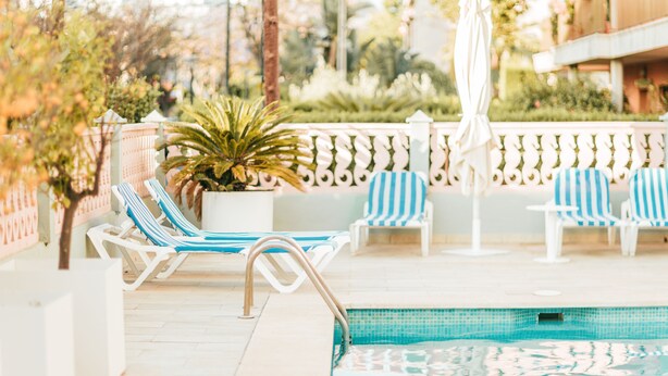 A poolside area with lounge chairs, a potted plant, and a white umbrella. - 4U Miranda - Adults Only (Calvia)