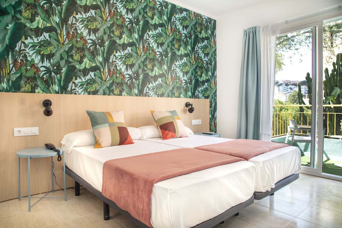 Una habitación de hotel con una cama grande, una mesita auxiliar pequeña y vistas a un jardín a través de una puerta corrediza de vidrio.