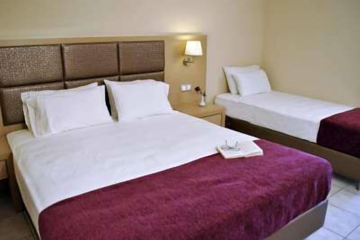 A hotel room with two beds, each with white bedding and a headboard. There is a nightstand with a lamp and a small table with a book and glasses.