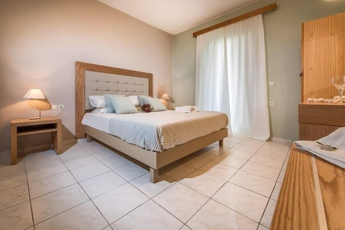 A bedroom with a bed, nightstands, a wooden dresser, and a window with curtains.