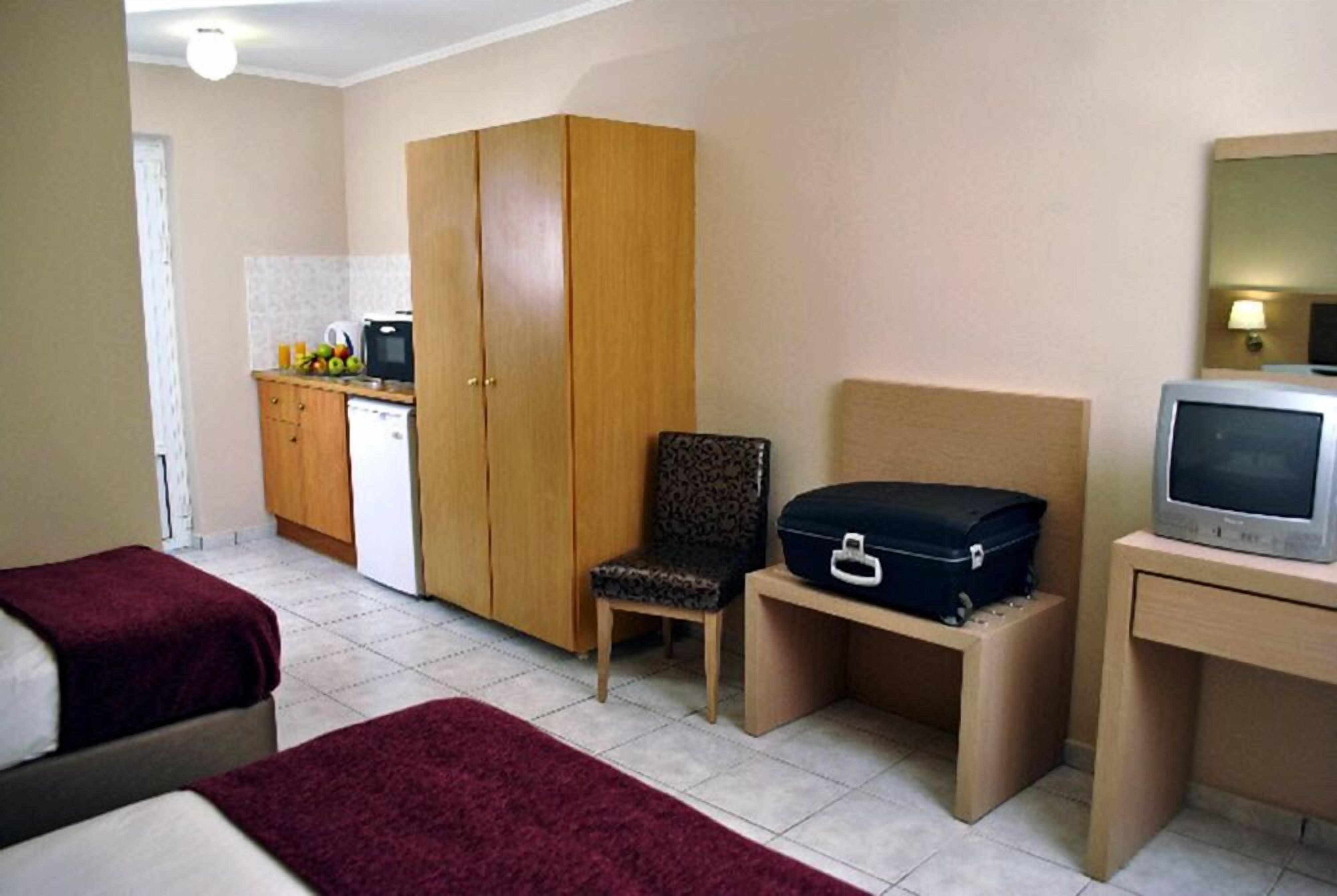 A hotel room with two beds, a wooden wardrobe, a small desk with a television, and a chair.