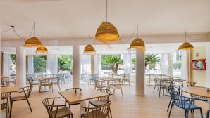 Un amplio comedor interior con varias mesas y sillas, ventanas grandes y lámparas colgantes de tejido.