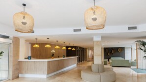 Un vestíbulo moderno con un mostrador de recepción, lámparas de mimbre colgantes y una zona de estar central.