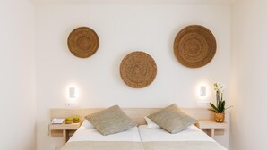 Un dormitorio ordenado con una cama, dos mesitas de noche y tres adornos de pared tejidos.