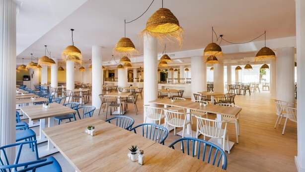 Un restaurante espacioso con techos altos, varias zonas de comedor y lámparas de mimbre colgantes.