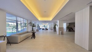Un vestíbulo espacioso con diseño moderno, que incluye una zona de estar con sofás y una mesita, ventanas amplias con vistas y un techo luminoso con iluminación empotrada.