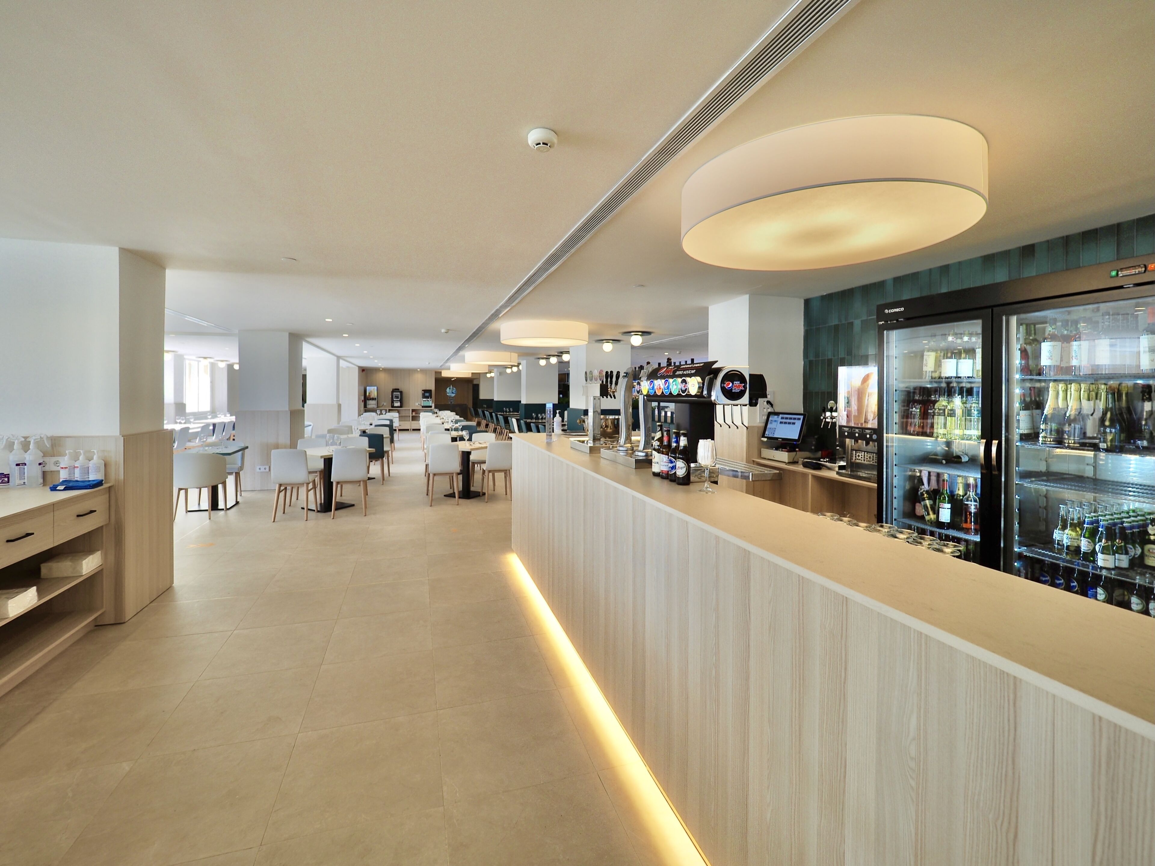 Un'area bar moderna con un bancone, posti a sedere e una vetrina refrigerata per bevande.