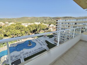 Un balcón con vista a una piscina y zona de estar, rodeado de vegetación y edificios.