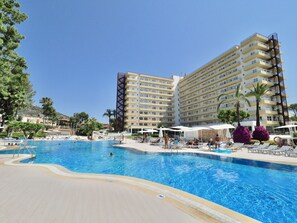 Un hotel con una amplia piscina, varios balcones y palmeras.