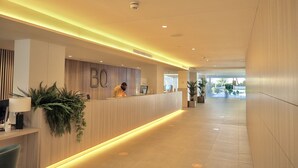 Una zona de recepción moderna con un mostrador de madera, un gran letrero 'BQ' y plantas en macetas.